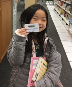 child holding a library card and books in the library