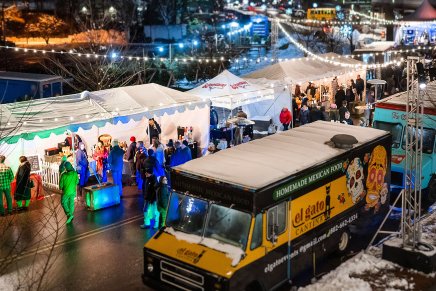 Food trucks and tents at a winter event with little lights.